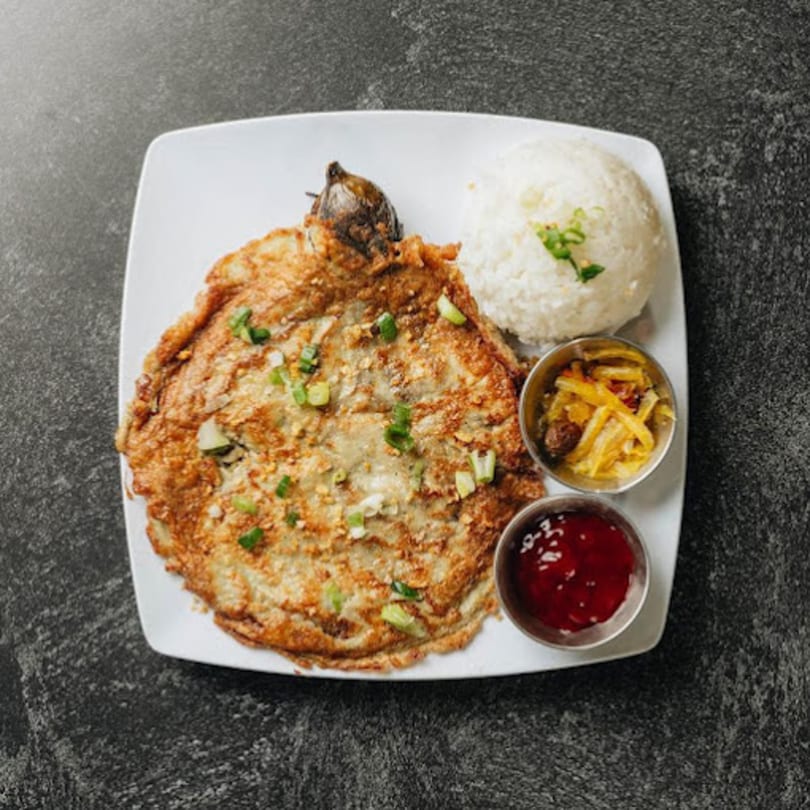 Filipino tortang talong with rice, pickled vegetables, and a red dipping sauce on a white plate.