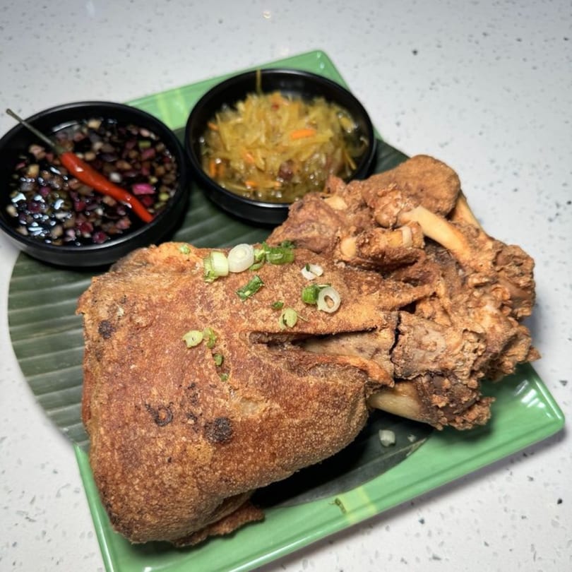 Crispy fried pork hock (Crispy Pata) with dipping sauces and pickled vegetables on a green plate.