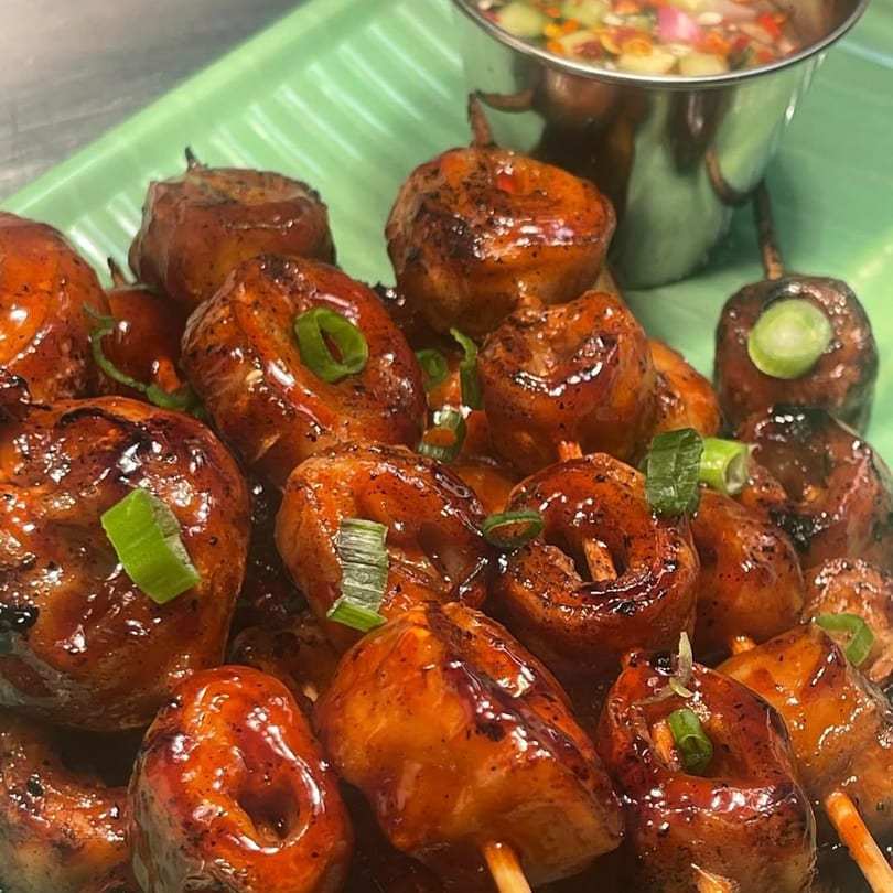Close-up of Filipino street food, skewered pork intestines (Isaw) with a dipping sauce.