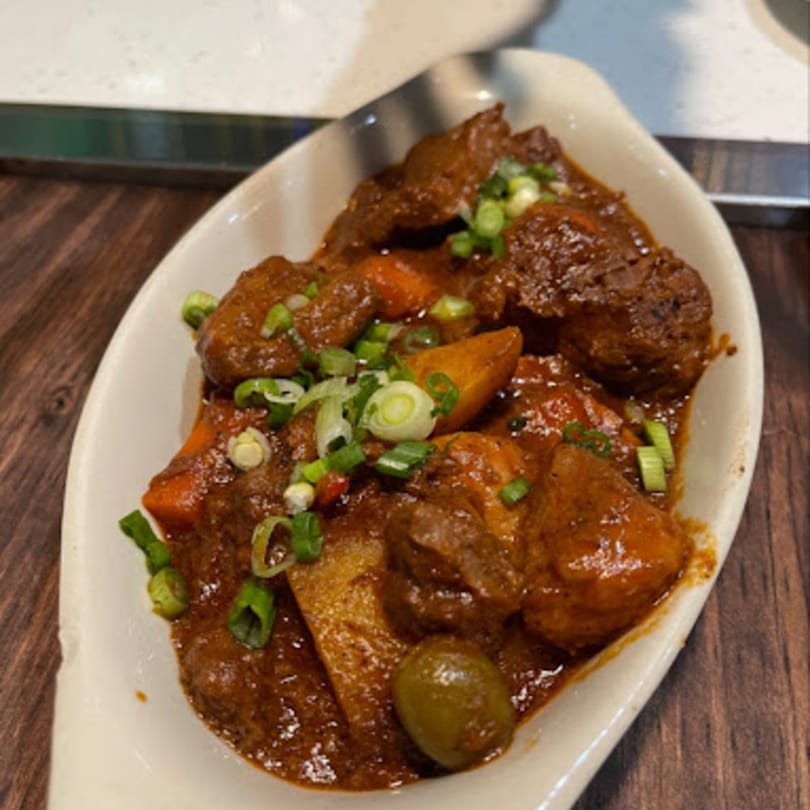 A white dish of Filipino Caldereta stew with meat, potatoes, carrots, olives, and green onions.