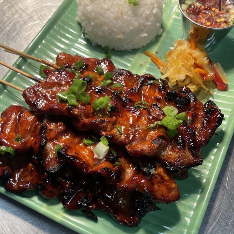 Tambayan Filipino Food's chicken skewers with rice, pickled vegetables, and dipping sauce on a green plate.