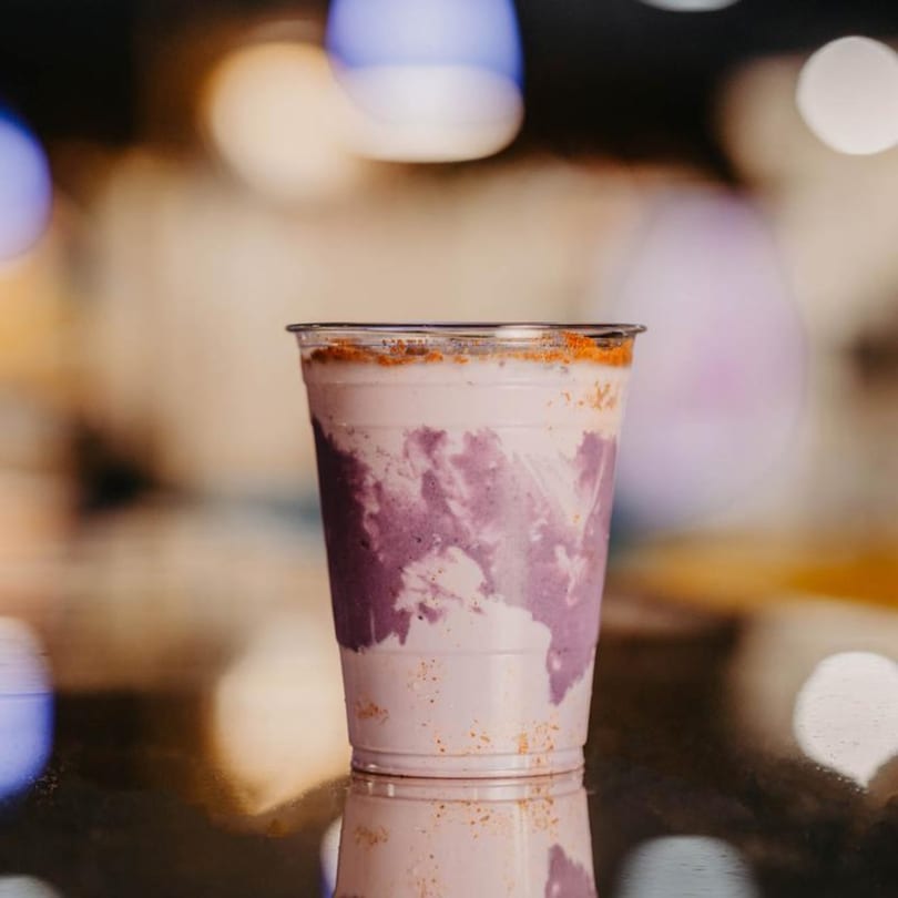 A purple and white ube drink in a clear plastic cup, topped with orange sprinkles.