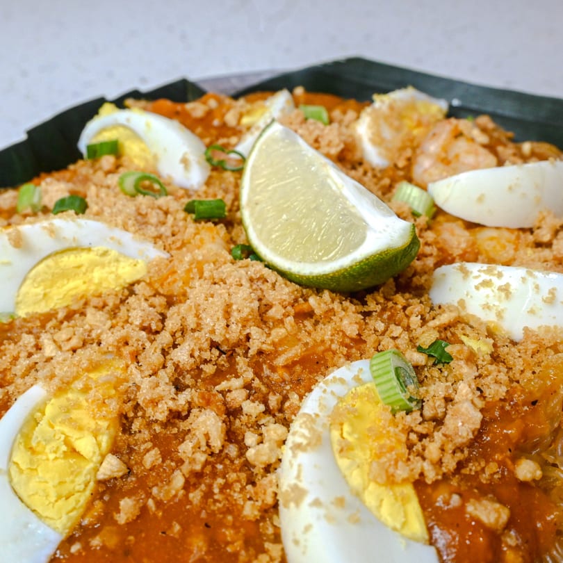 Pancit Palabok with orange sauce, crushed chicharon, sliced eggs, green onions, and lime.