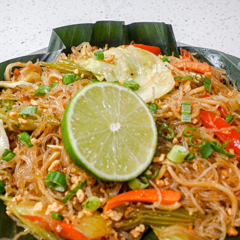 Close-up of glass noodles with vegetables, peanuts, and a lime slice, served in a banana leaf.