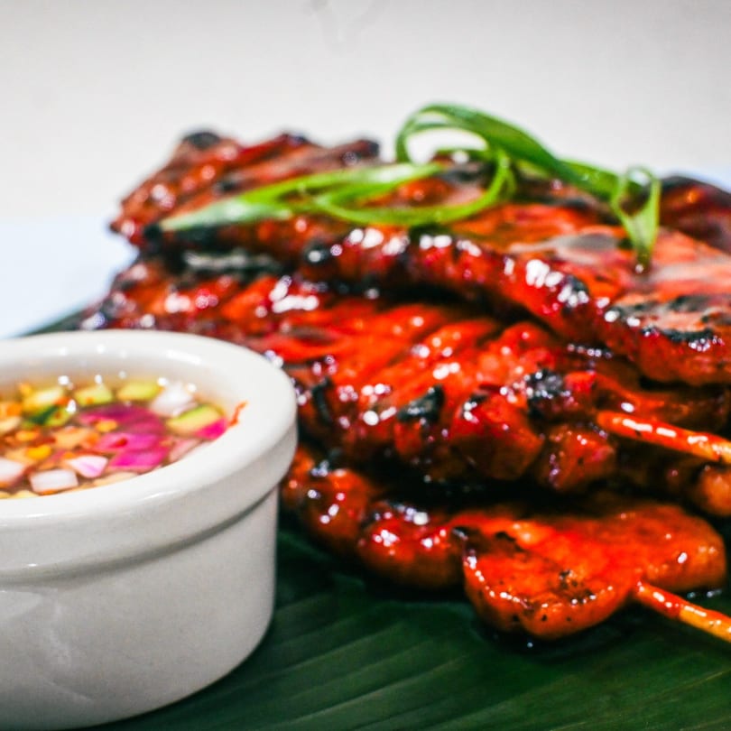 Grilled Filipino pork skewers (pork BBQ) with green onions and a side of dipping sauce.